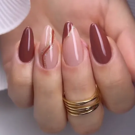 Mão com unhas amendoadas em soft gel na cor marrom terracota, uma delas com traço dourado.