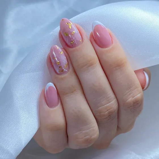 Mão com unhas em soft gel nude rosado, com folha dourada e francesinha branca na ponta.